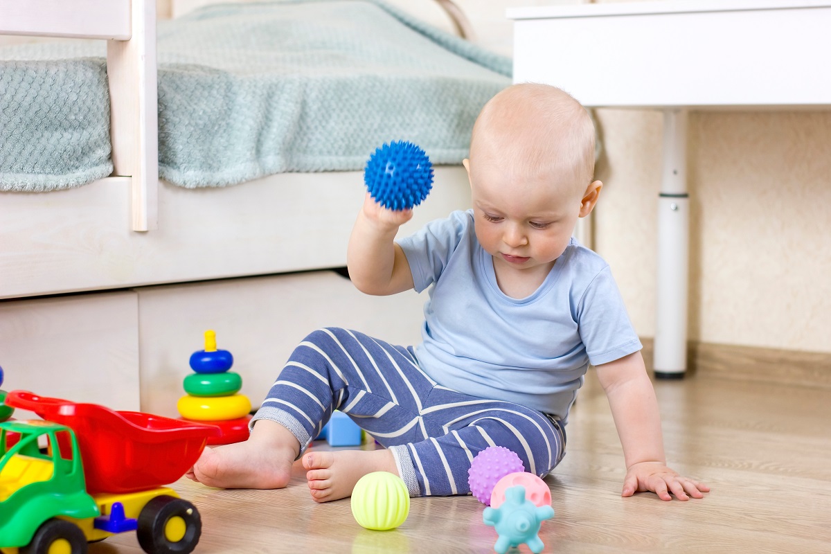 Băiețelul se joacă pe podea cu câteva mingi