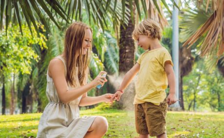 O mamă care îi aplică băiețelului ei un spray împotriva insectelor în timp ce se află într-o vacanță într-un loc tropical
