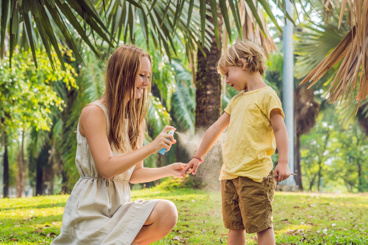 O mamă care îi aplică băiețelului ei un spray împotriva insectelor în timp ce se află într-o vacanță într-un loc tropical