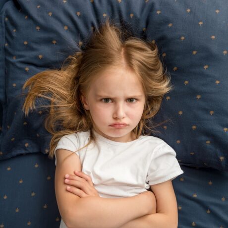 Fetița stă supărată pe patul de dormitor
