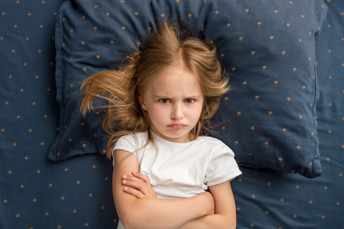Fetița stă supărată pe patul de dormitor