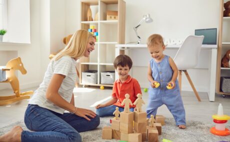 O mămică ce se joacă cu doi copii într-o cameră plină cu jucării de lemn pentru a ilustra modul în care jocurile pot să îmbunătățească dispoziția unui copil