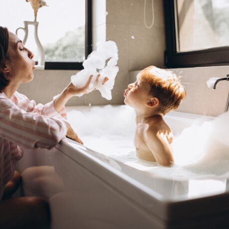 O mămică care stă în fața unei căzi în care se află un copilaș care își face baie cu spumă