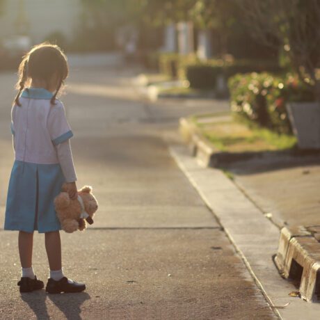 O fetiță care se plimbă singură pe stradă, cu un ursuleț în brațe