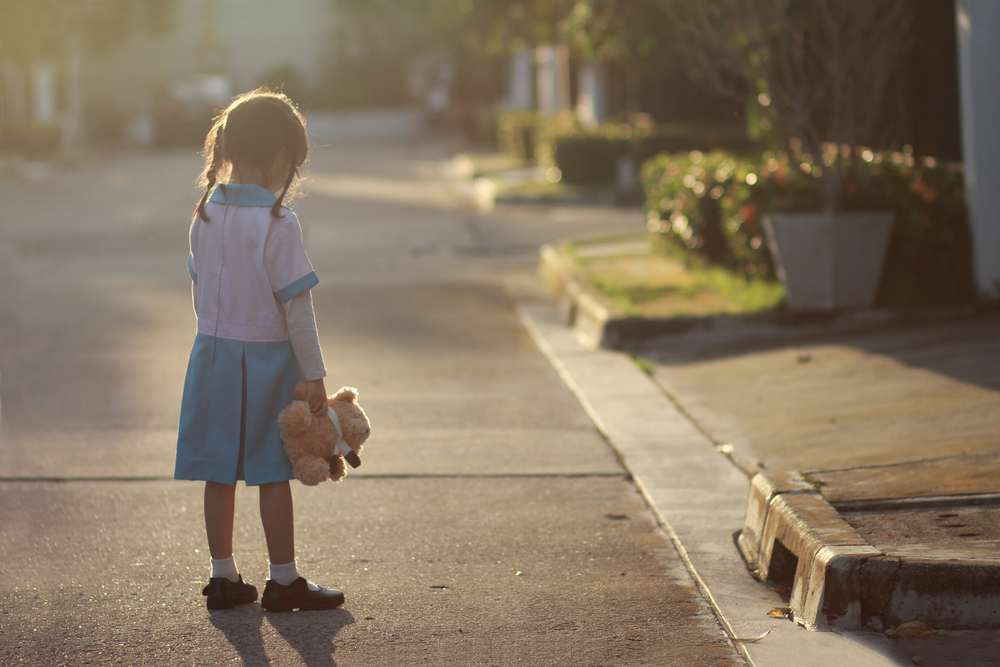 O fetiță care se plimbă singură pe stradă, cu un ursuleț în brațe