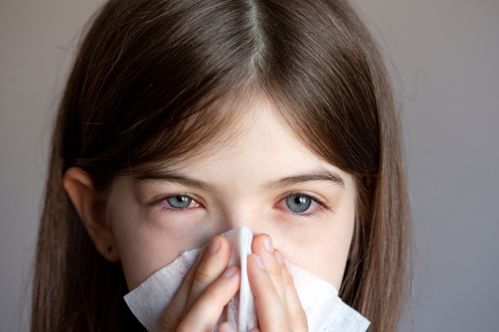 O fetiță cu ochii inflamați, care își suflă nasul
