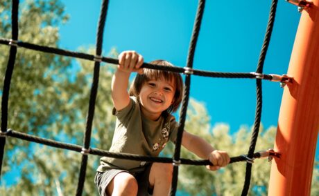 Un băiețel care se cațără pe o funie în parc pentru a ilustra una dintre cele mai periculoase activități pentru copii