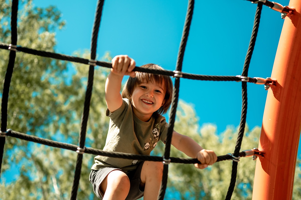 Un băiețel care se cațără pe o funie în parc pentru a ilustra una dintre cele mai periculoase activități pentru copii