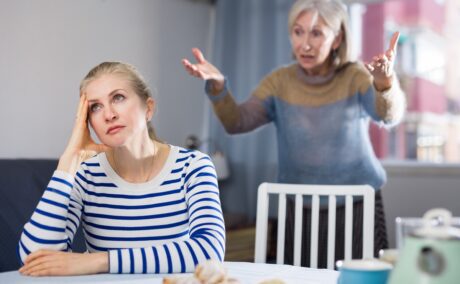 O mamă care își ceartă fiica, o femeie deja adultă, care stă la masă și își sprijină capul în mâini