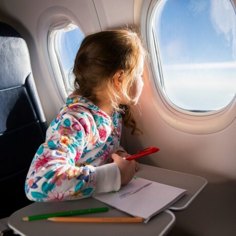 Fetița desenează și se uită pe geamul avionului
