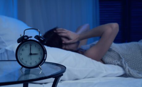 Femeie care nu poate să doarmă într-un pat cu un ceas în prim-plan