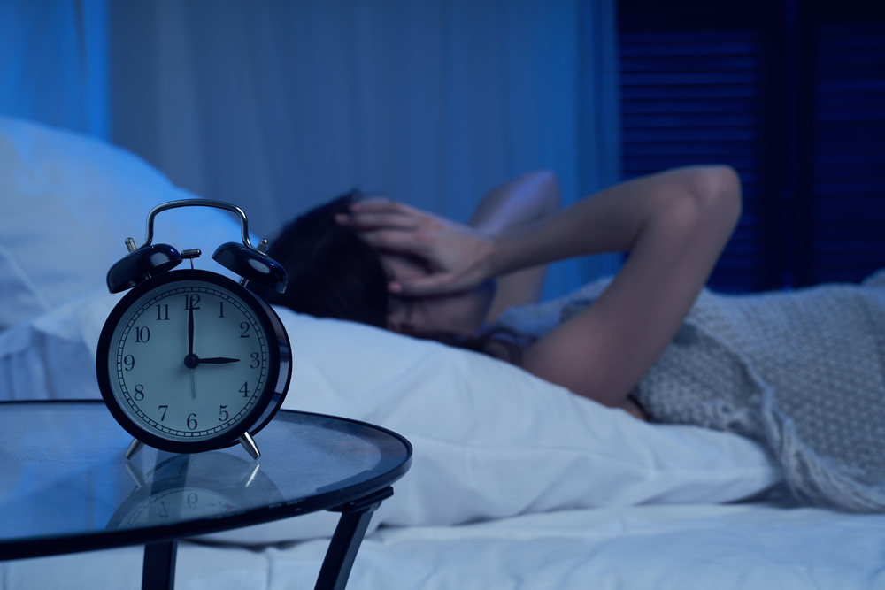 Femeie care nu poate să doarmă într-un pat cu un ceas în prim-plan