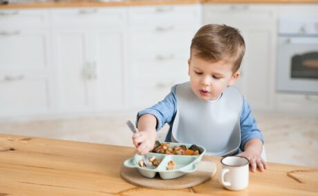 Un băiețel care stă la masă și mânâncă alimente care ar putea fi nesigure pentru copii