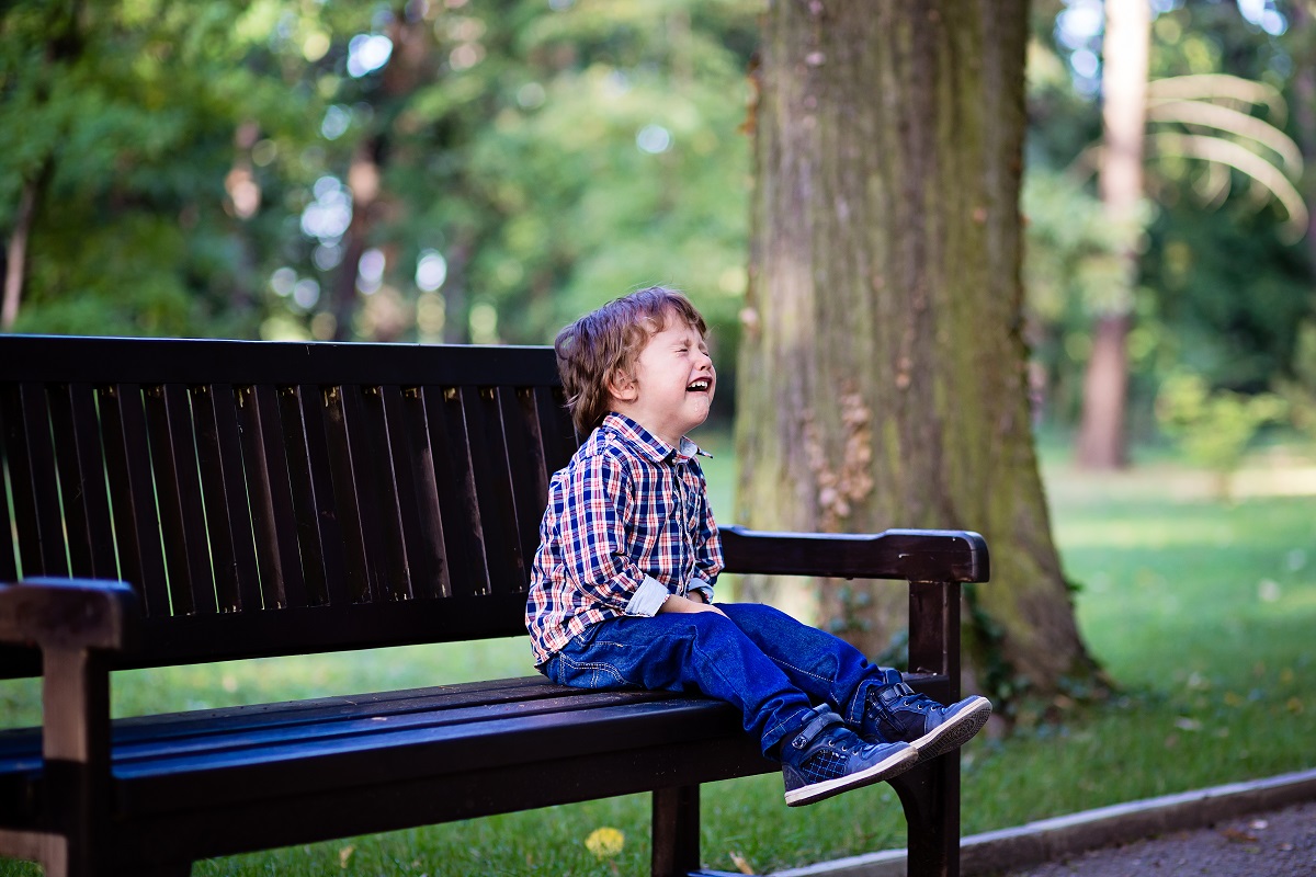 Băiețel stă pe bancă și plânge
