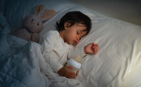 Un toddler care doarme în pătuț în timp ce ține biberonul în mână
