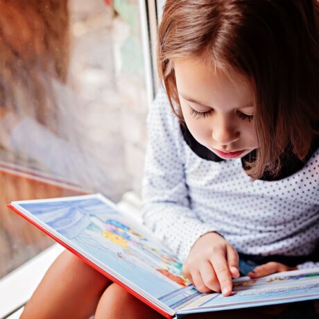 Fetiță stă jos și citește dintr-o carte