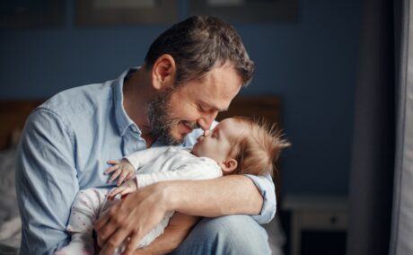 Un tătic care își ține bebelușul în brațe și îl privește în ochi pentru a forma o legătură de atașament