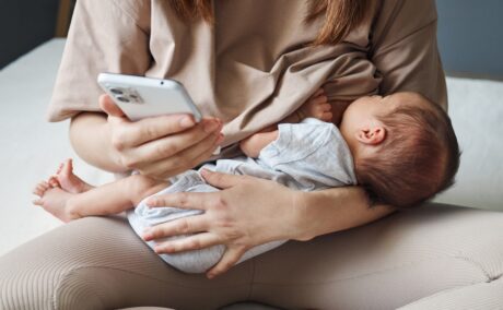 O femeie care își alăpteazî bebelușul și se uită pe telefon