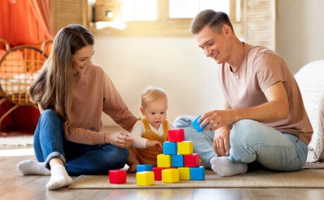 o mamă și un tătic care se joacă cu bebelușul pe un covor și construiesc un turn din cuburi colorate