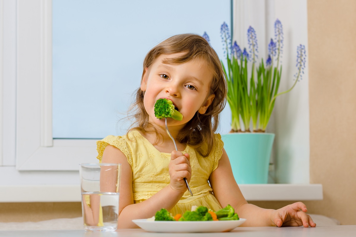 O fetiță care stă la masă și mănâncă broccoli dintr-o farfurie