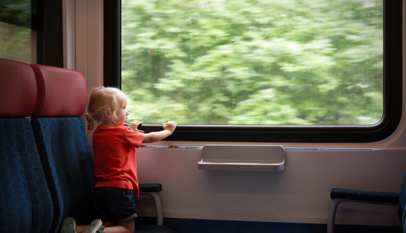 Copil stă și se uită pe geamul trenului