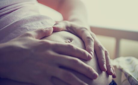 Femeie însărcinată cu mâinile pe burtă într-o cameră luminoasă