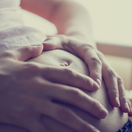 Femeie însărcinată cu mâinile pe burtă într-o cameră luminoasă