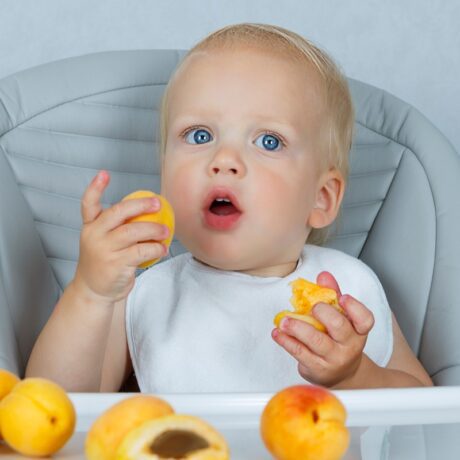 Un bebeluș care stă la măsuță și consumă bucăți mici de caise