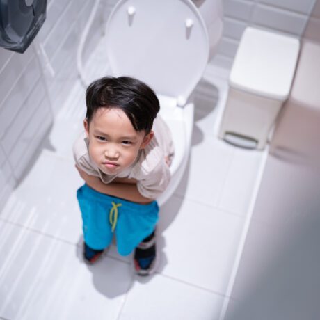 Băiat care stă pe toaletă și se uită în sus pe un fundal deschis la culoare