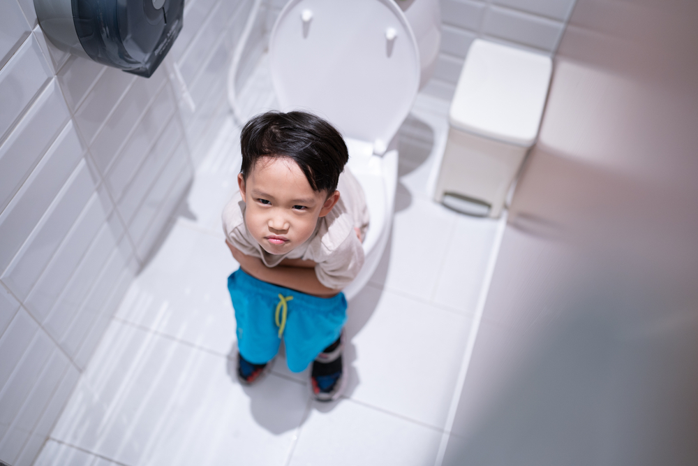 Băiat care stă pe toaletă și se uită în sus pe un fundal deschis la culoare