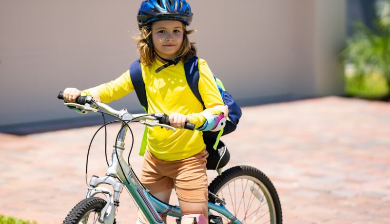 Un băiețel care poartă echipament de protecție și merge pe prima lui bicicletă