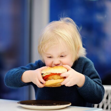 Copil mănâncă un hamburger