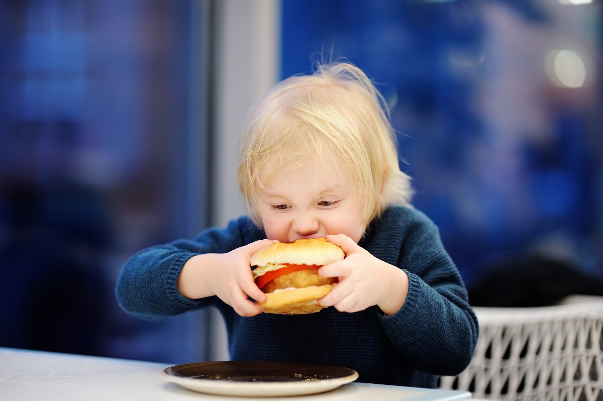 Copil mănâncă un hamburger