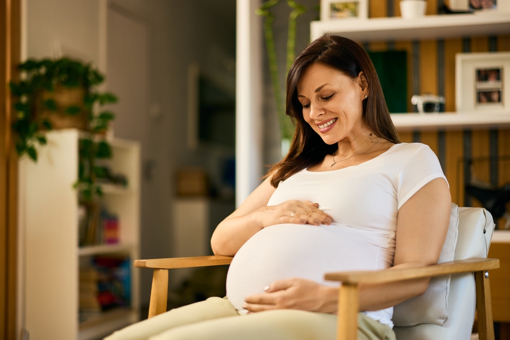 femeie frumoasă însărcinată care stă pe un fotoliu și zâmbește