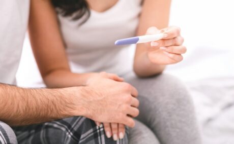mână de femeie și mână de bărbat pe un fundal deschis la culoare cu un test de sarcină
