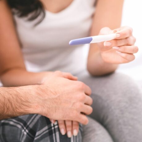 mână de femeie și mână de bărbat pe un fundal deschis la culoare cu un test de sarcină