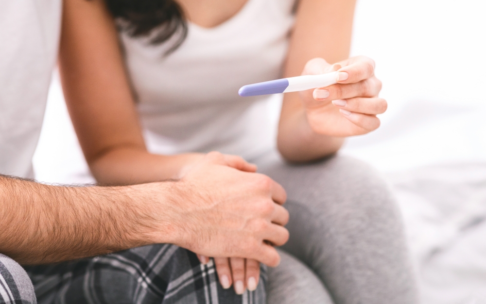 mână de femeie și mână de bărbat pe un fundal deschis la culoare cu un test de sarcină