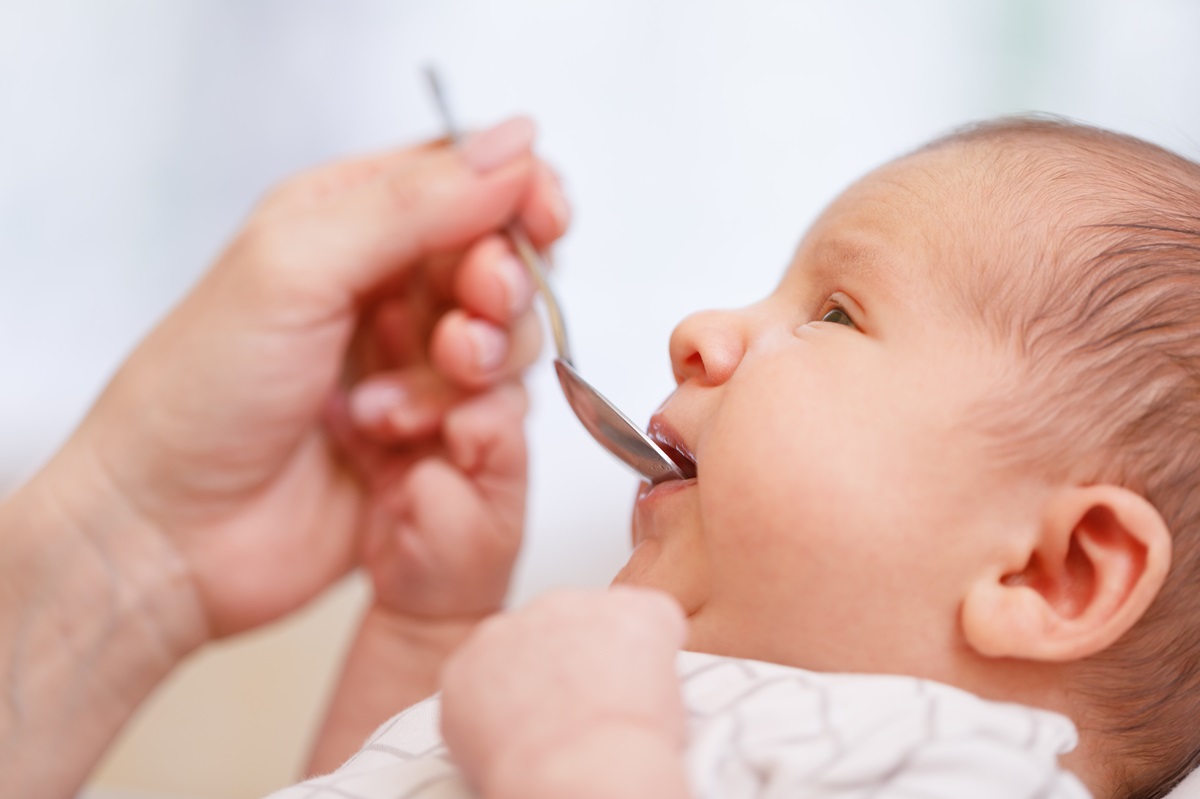 O mămică care îi oferă copilului ei o linguriță cu vitamina C