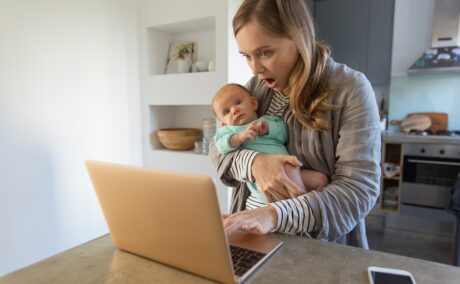 Mama cu bebelușul în brațe se uită uimită pe laptop