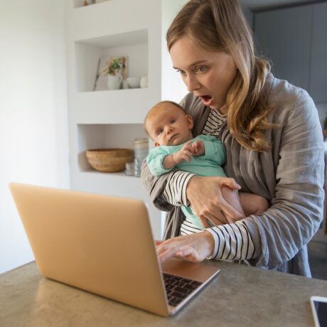 Mama cu bebelușul în brațe se uită uimită pe laptop