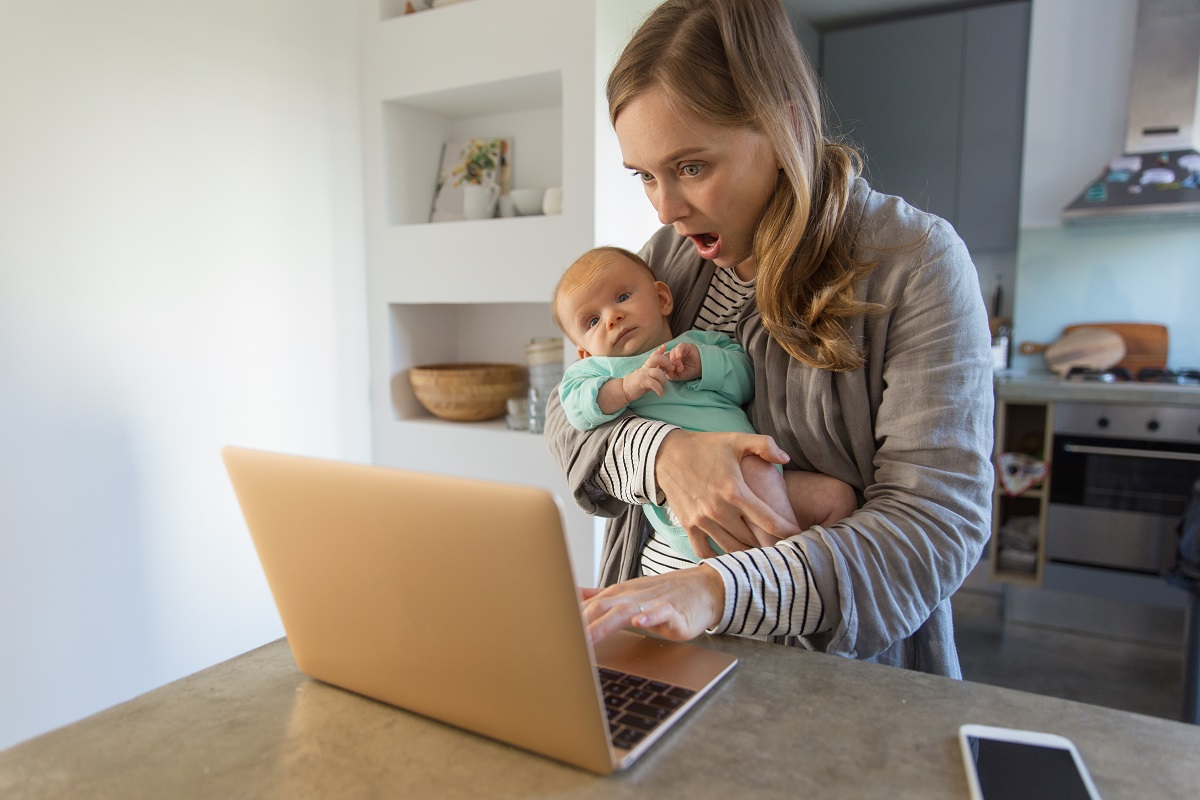 Mama cu bebelușul în brațe se uită uimită pe laptop