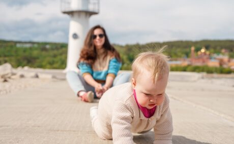 Mama supraveghează bebelușul care merge în patru labe să exploreze locul