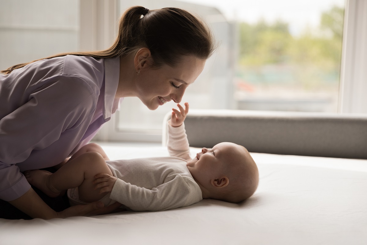 Mama vorbește cu bebelușul întins pe pat