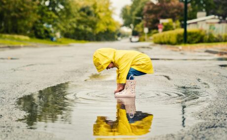 Copilul se joacă într-o baltă, în timp ce afară plouă