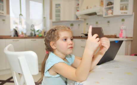 Fetița stă la masa și se uită pe telefon