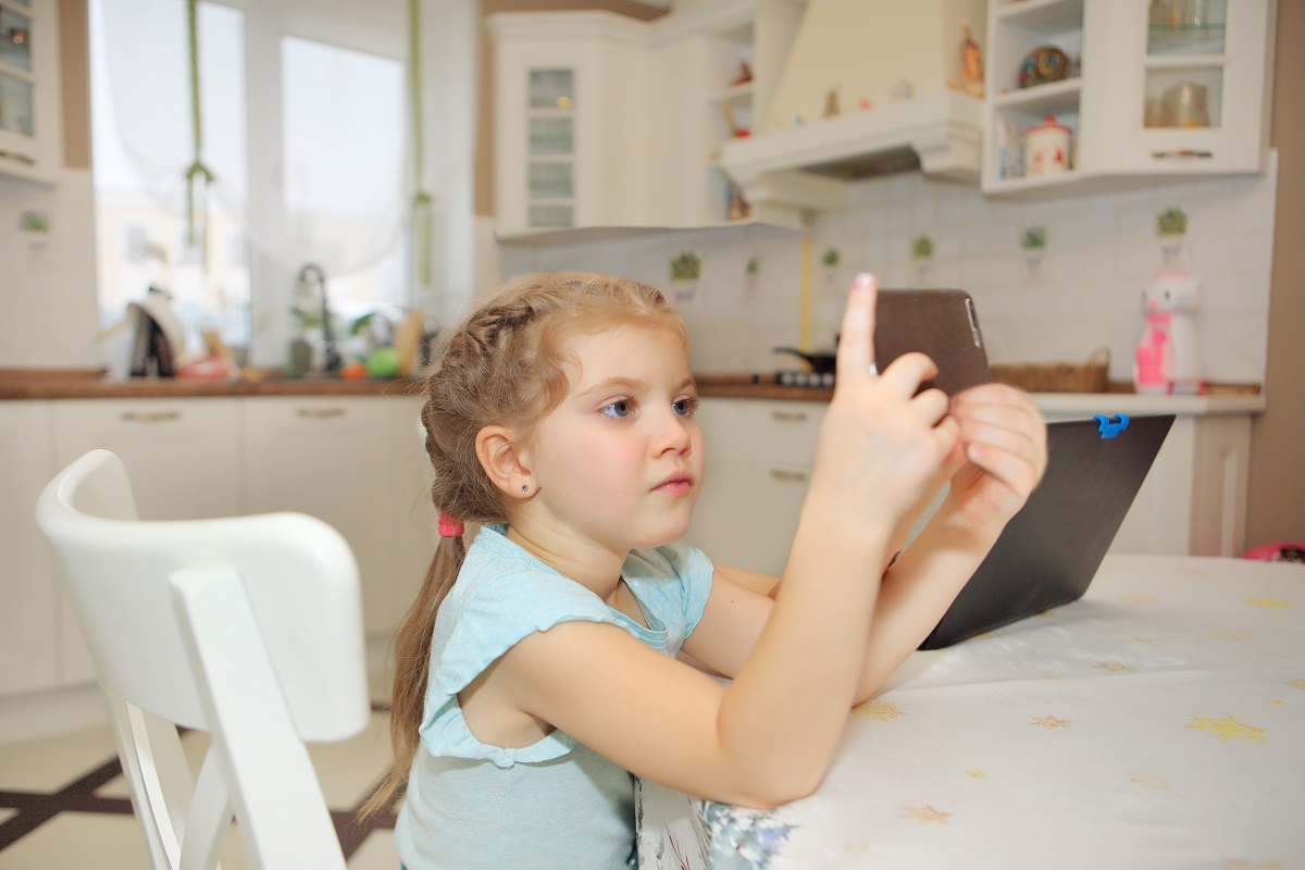 Fetița stă la masa și se uită pe telefon