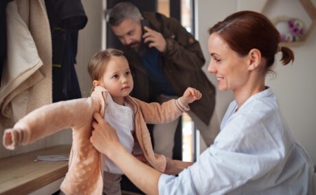Mama își ajută fetița să se îmbrace de școală, iar tată se pregătește să iasă din casă