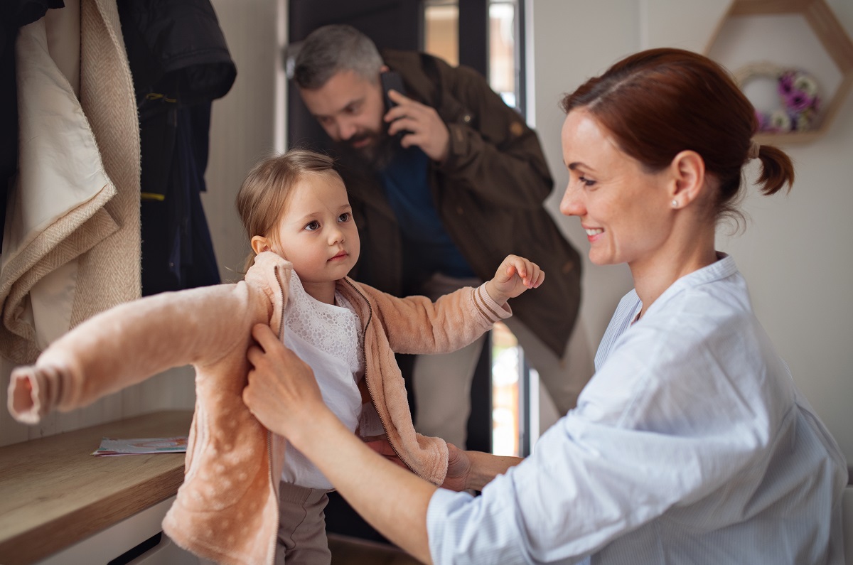 Mama își ajută fetița să se îmbrace de școală, iar tată se pregătește să iasă din casă