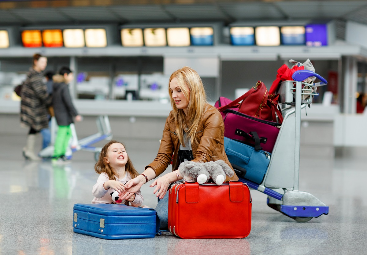 Fetiță stă pe jos prin aeroport și plânge, iar mama încearcă să o calmeze