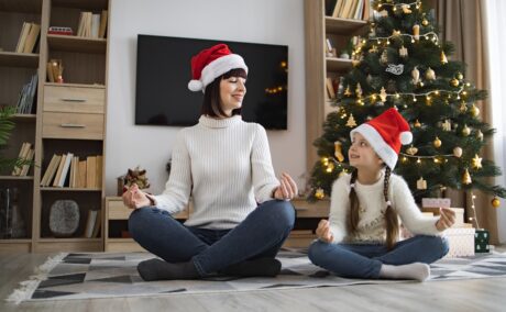 Mama și fetița stau în poziție de yoga în fața bradului